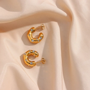 Detail of gold C-shaped earrings with inlaid zircons on soft pink satin fabric