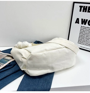 Detail shot of off-white canvas messenger bag with a white fluffy pompom charm on denim