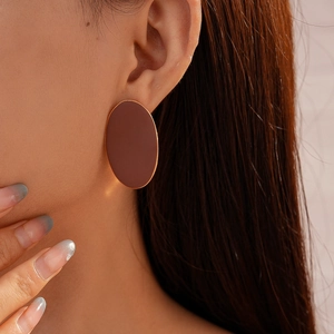 Close-up of model wearing matte brown oval earrings with gold trim in a retro style