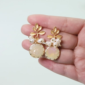 Detail of leaf-shaped gold earrings with freshwater pearls and round mother of pearl charms