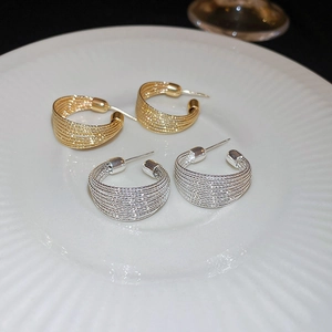 Macro shot of gold and silver C-shaped woven metal earrings on white ceramic plate