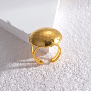 Macro detail of golden dome ring featuring hammered texture on white plaster background