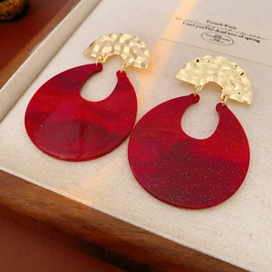 Detail of dark red resin and hammered gold metal earrings in a luxury display box