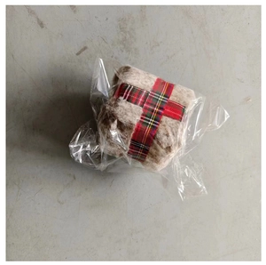 Detail of plush Christmas gift box ornament with red plaid ribbon in protective packaging