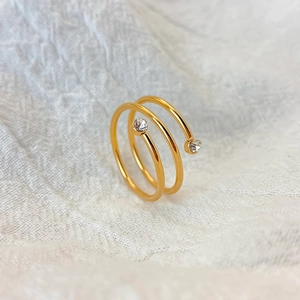 Makroaufnahme eines goldenen Spiralrings mit Zirkonia auf weißem strukturiertem Stoff