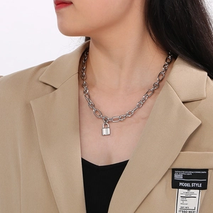 Close-up of a silver padlock pendant on a chunky chain necklace worn with a suit