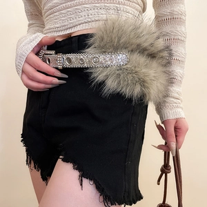 Détail d'une ceinture en strass argentée avec pompons en fourrure sur short en jean