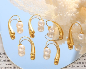 Close-up of three pairs of elegant gold teardrop earrings with pearls on a mirror tray