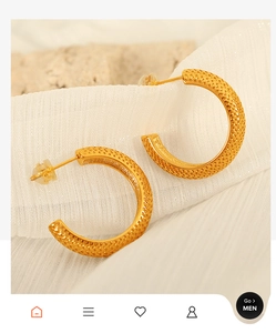 Detailed view of gold-tone C-shaped earrings with textured mesh pattern on soft white fabric