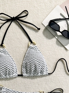 Detail of white crochet bikini top with black straps and resin ring accents on beige rug