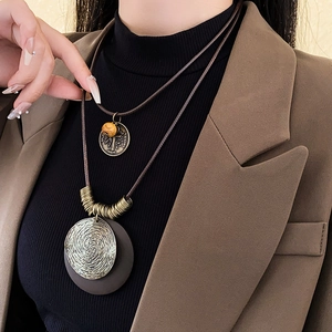 Détail de colliers en cuir vintage avec breloques en métal gravées et perles sur un mannequin