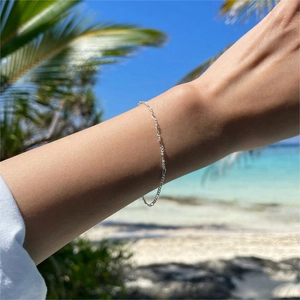 Detail of 925 sterling silver Figaro chain bracelet worn on a sunny beach background