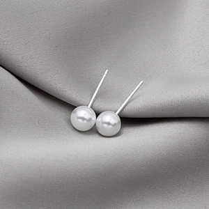 Macro shot of elegant round cream-white pearl earrings on smooth grey silk fabric