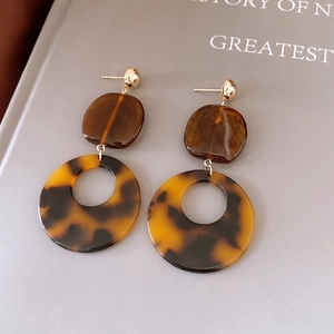 Détail de boucles d'oreilles rondes en résine écaille sur fond de magazine gris