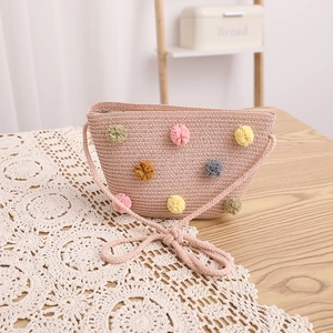 Detail of pink straw shoulder bag featuring colorful pom poms and woven texture