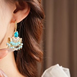 Gros plan d'une boucle d'oreille dorée avec gemme bleue, perles et pompons en perles bleues