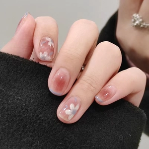 Short press-on nails with pink blush gradient, white camellia pattern, and blue tip edges