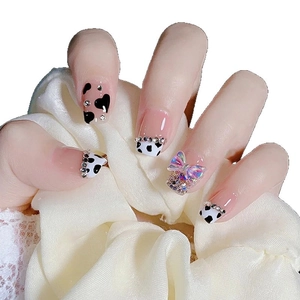 Press-on nails featuring black and white cow print with rhinestone bow and aurora gems