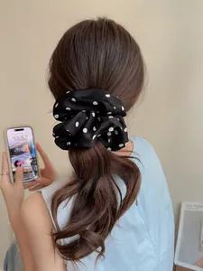 Detail of a large black and white polka dot satin scrunchie on a ponytail