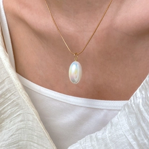 Close-up of elegant gold chain necklace with iridescent white pear-shaped pendant