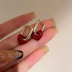 Golden oval hoop earrings featuring dark red heart drops held by hand in soft light