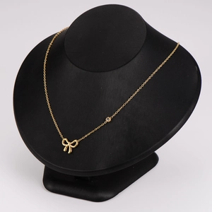 Elegant gold bow pendant necklace with a round gemstone on a black jewelry display stand