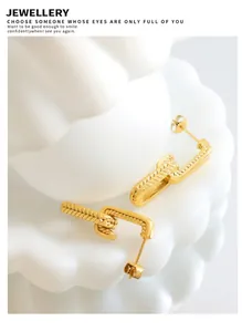 Close-up of gold chain-link U-shape earrings with dot texture on white ripple background