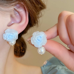 Détail de boucles d'oreilles rose bleu clair avec perle blanche et finition résine