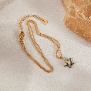 Macro detail of gold stainless steel star necklace with abalone shell and evil eye motif