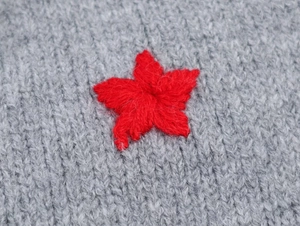 Detailed close-up of grey knit hooded cardigan with red star-shaped embroidery detail