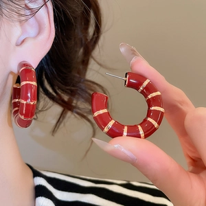 Close-up of red enamel C-shape hoop earrings with gold stripes worn by a model