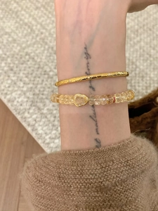 Détail d'un bracelet en perles avec pendentif hulu et jonc doré texturé sur le poignet