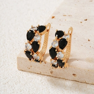 Detailed close-up of golden teardrop earrings with black and white crystals on stone