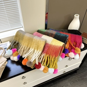 Chunky rainbow plaid scarf with colorful pom-pom tassels on a white vanity desk