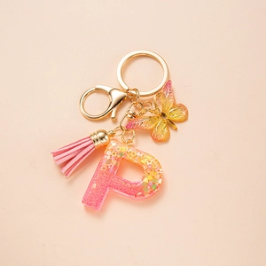 Detail of pink resin letter P keychain with glitter, tassel and butterfly pendant