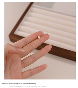 Close-up of a gold sun stud earring with a zircon center held on a fingertip for scale