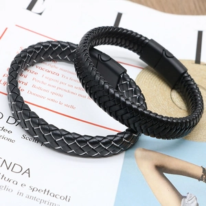 Set of two black braided leather bracelets with matte magnetic clasps on a magazine