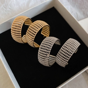 Detail view of gold and silver C-shaped mesh earrings with beaded metal texture