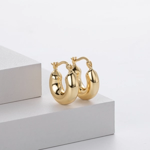 Detailed view of glossy golden hollow hoop earrings on a clean white geometric platform
