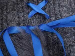 Close-up of dark gray plush knit fabric with royal blue satin ribbon detail and soft texture