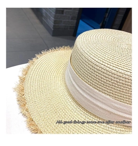 Detailed close-up of straw beach hat featuring frayed brim and cream decorative ribbon