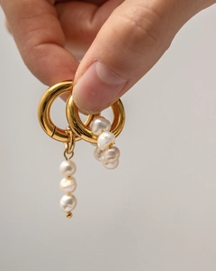 Detailaufnahme von goldenen Creolen mit barocken Perlenanhängern aus Edelstahl in der Hand