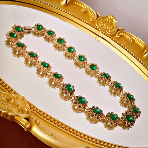 Dettaglio di un bracciale vintage dorato con pietre verde smeraldo su uno specchio