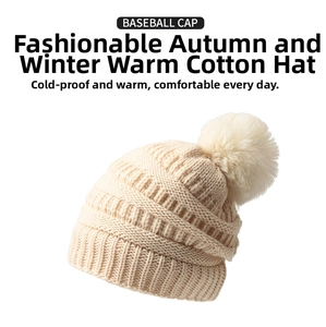 Détail du bonnet en maille crème avec motifs de torsades et un gros pompon en fourrure douce