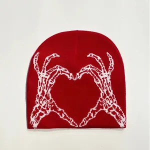 Close-up detail of red knitted beanie featuring a white heart-shaped skeleton hands jacquard
