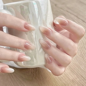 Close-up of nude gradient almond press-on nails with glossy finish on hands holding a cup