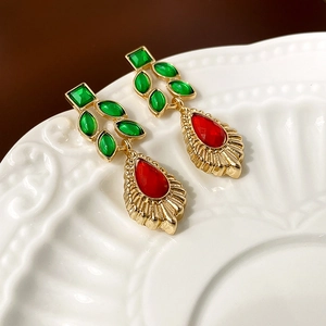 Macro detail of vintage gold earrings with green leaf gems and red teardrop pendant