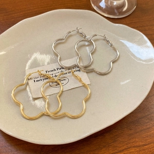 Minimalist hollow flower hoop earrings in gold and silver finish on white ceramic tray