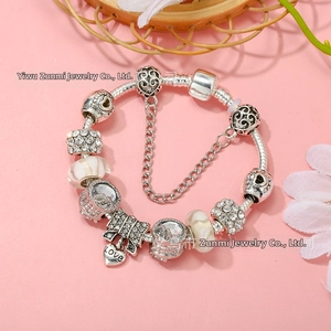Macro detail of silver charm bracelet with love heart pendant and pink glass beads