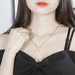 Close-up of a gold X-shaped pendant necklace with sparkling rhinestones on a model